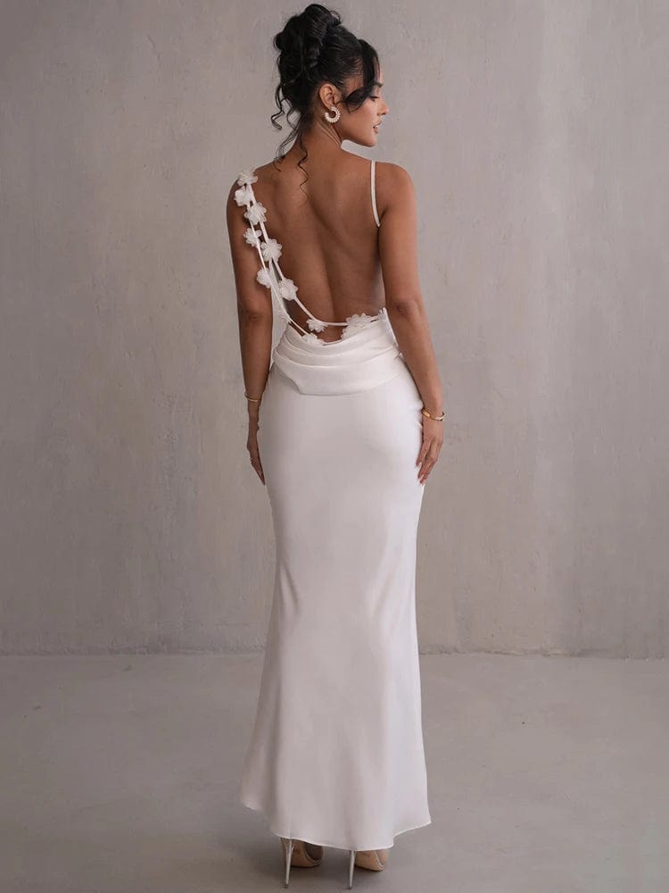 Robe longue dos nu blanche avec bretelles spaghetti pour soirée chic ou mariage, silhouette trapèze et détail fleuri.