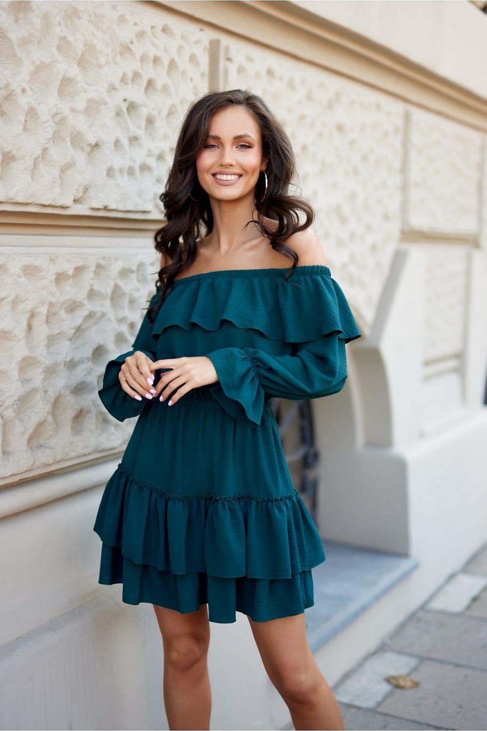 Robe de cocktail verte courte à volants superposés avec manches longues et épaules dénudées, style élégant et festif.