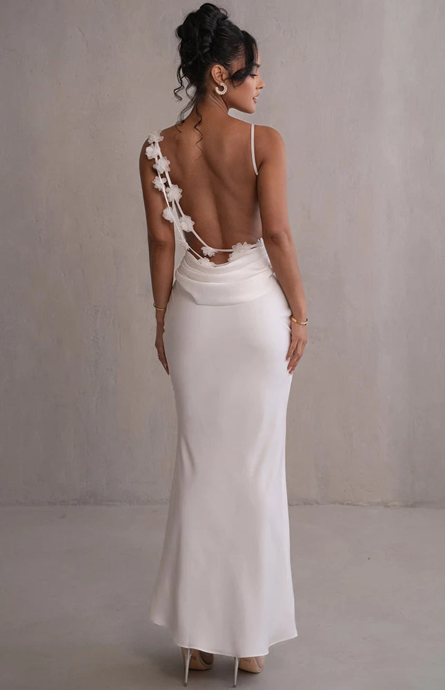 Robe longue dos nu blanche avec bretelles spaghetti pour soirée chic ou mariage, silhouette trapèze et détail fleuri.