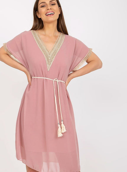 Robe rose courte casual chic avec détails en crochet et ceinture à pompons pour une tenue estivale ou de plage.