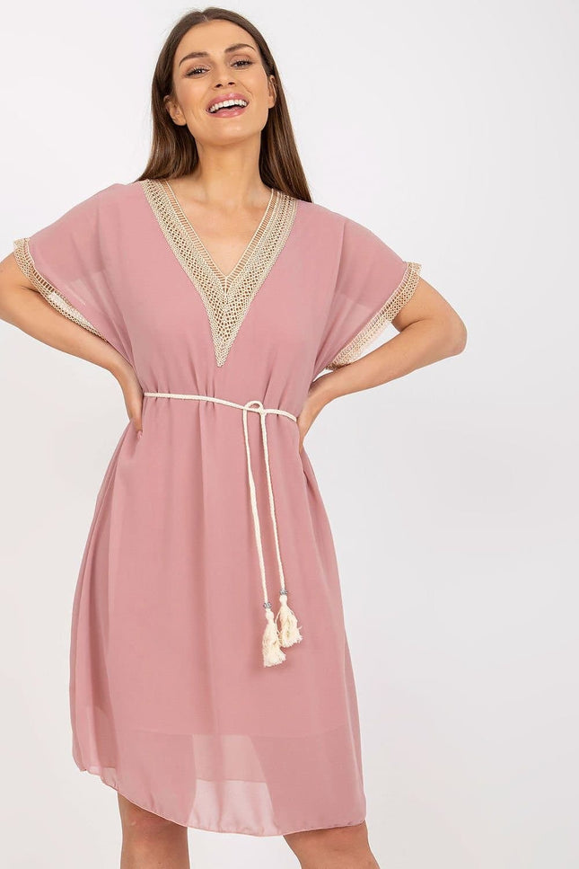 Robe rose courte casual chic avec détails en crochet et ceinture à pompons pour une tenue estivale ou de plage.