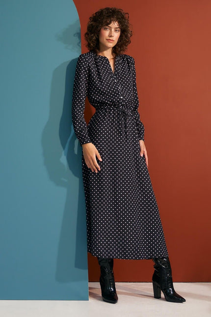 Robe noire à pois longue avec manches longues et ceinture, style vintage chic et élégante pour soirée ou événement.