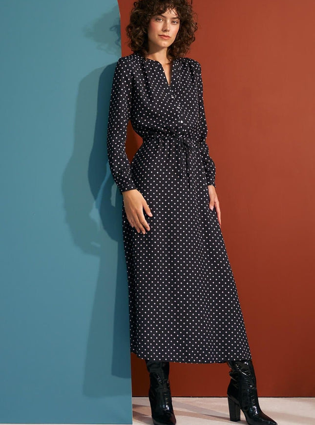 Robe noire à pois longue avec manches longues et ceinture, style vintage chic et élégante pour soirée ou événement.